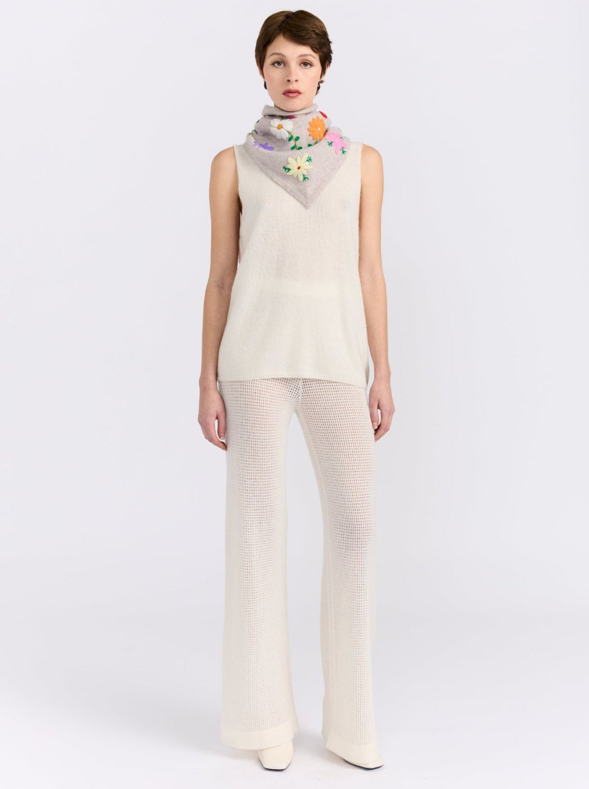 Model wearing the MANDKHAI New Beige embroidered triangle cashmere scarf styled around the neck.