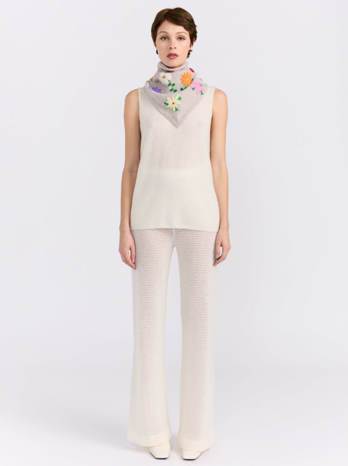 Model wearing the MANDKHAI New Beige embroidered triangle cashmere scarf styled around the neck.