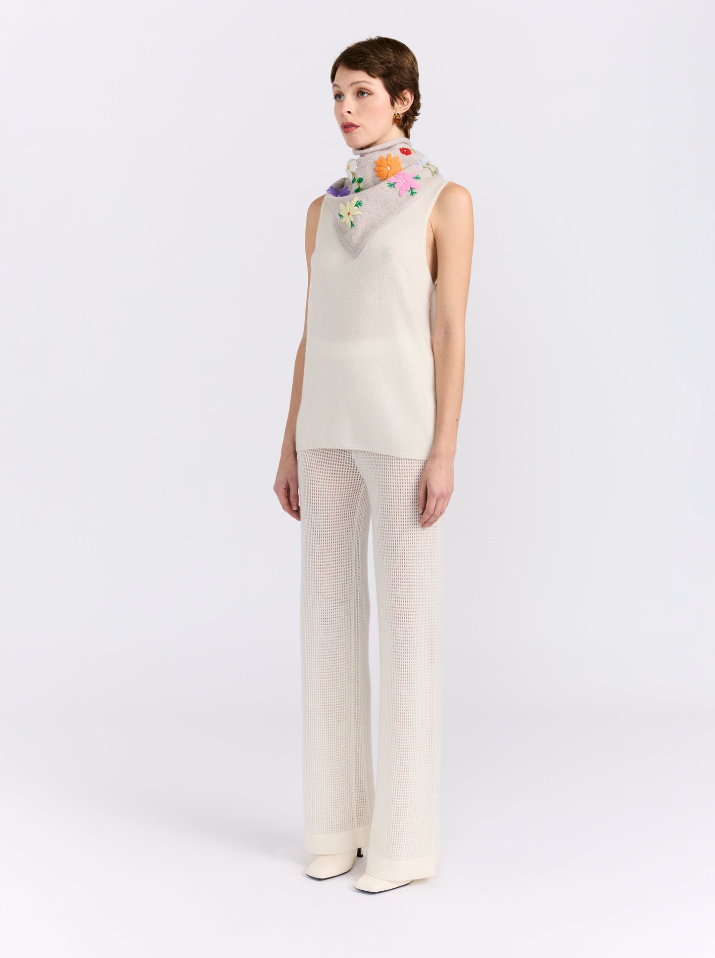 Model wearing the MANDKHAI New Beige embroidered triangle cashmere scarf styled around the neck.
