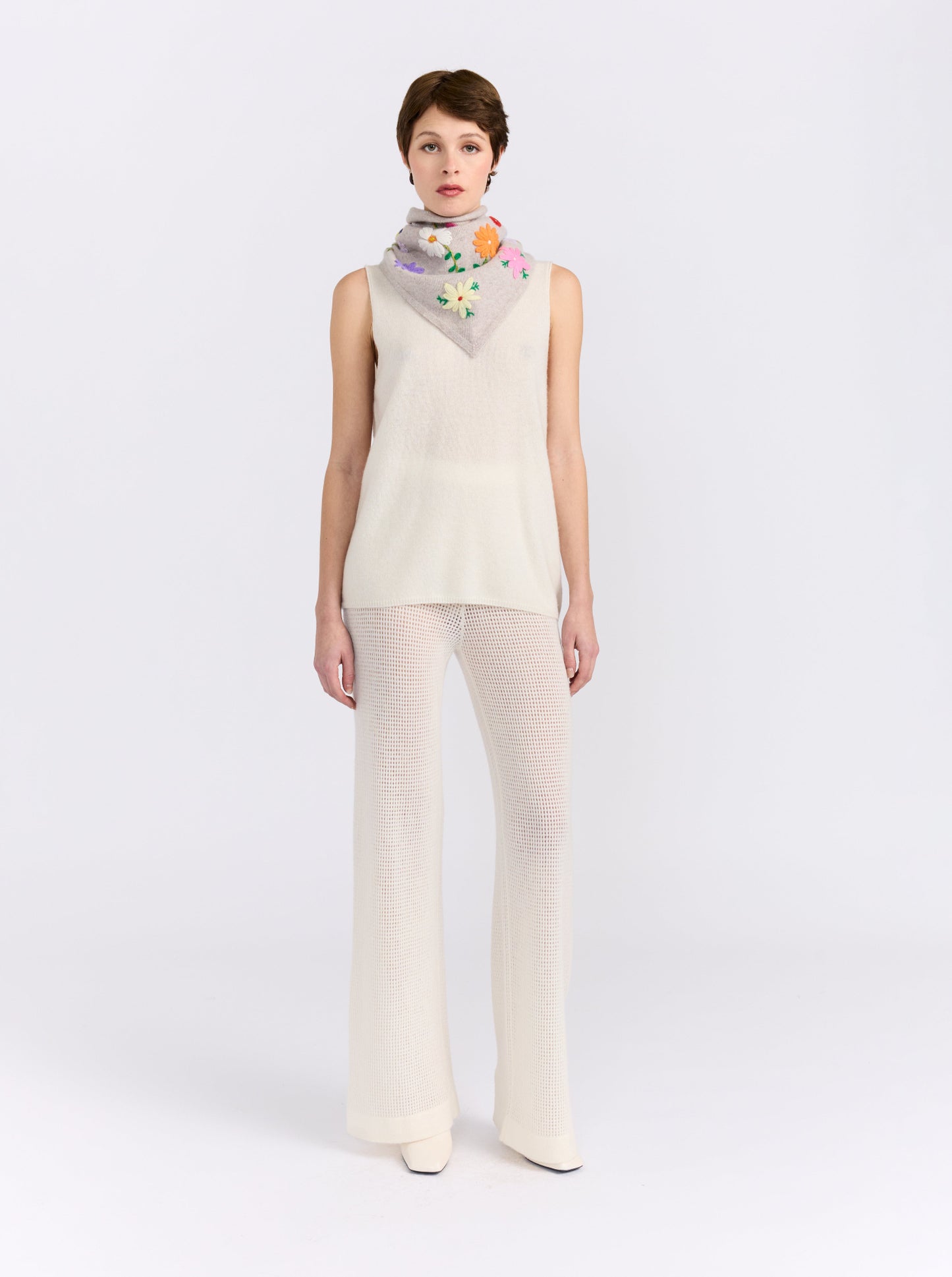 Model wearing the MANDKHAI New Beige embroidered triangle cashmere scarf styled around the neck.