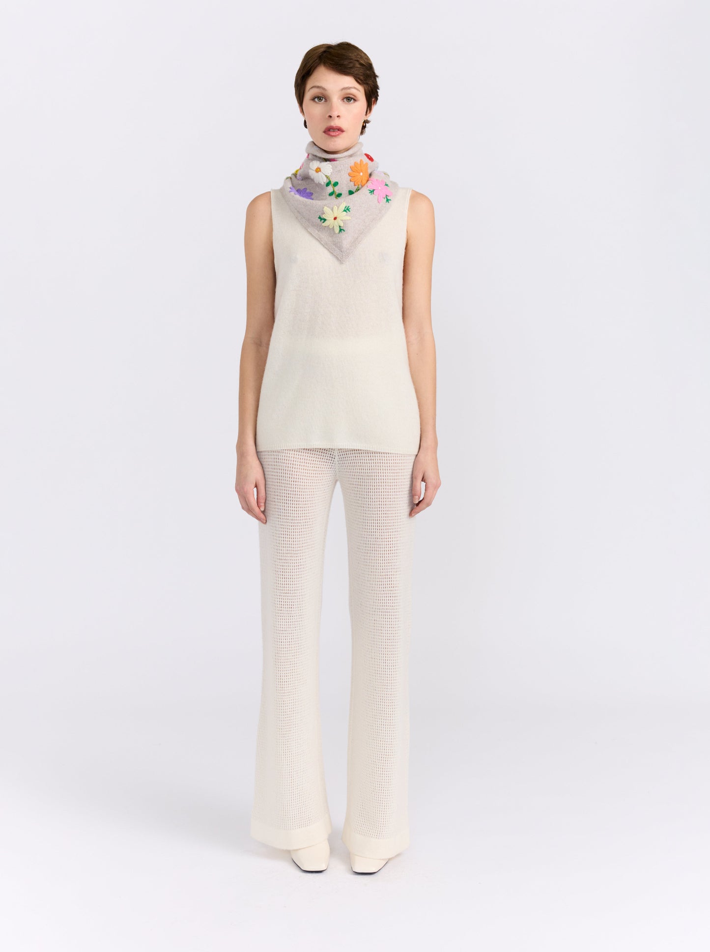 Model wearing the MANDKHAI New Beige embroidered triangle cashmere scarf styled around the neck.