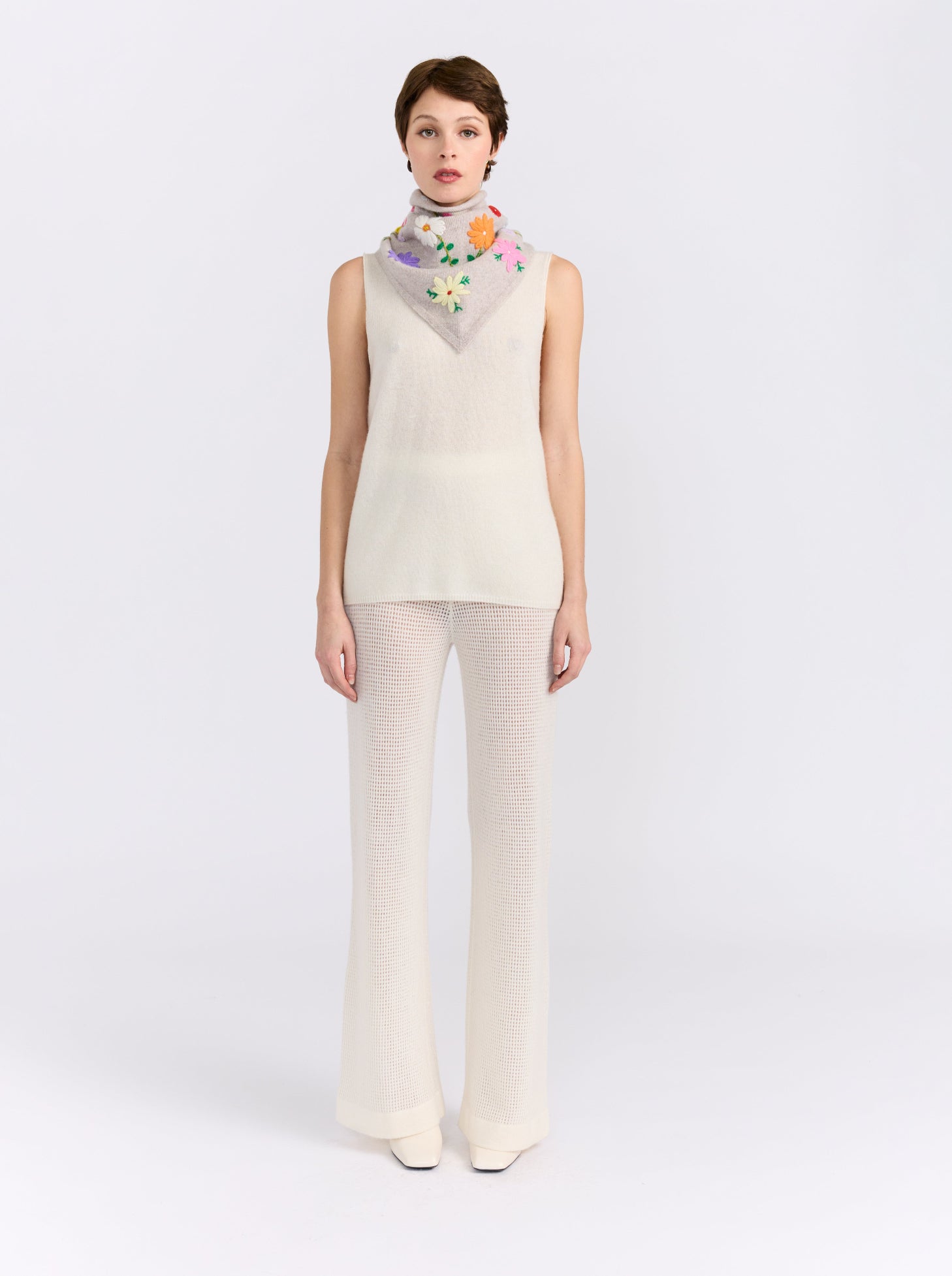 Model wearing the MANDKHAI New Beige embroidered triangle cashmere scarf styled around the neck.