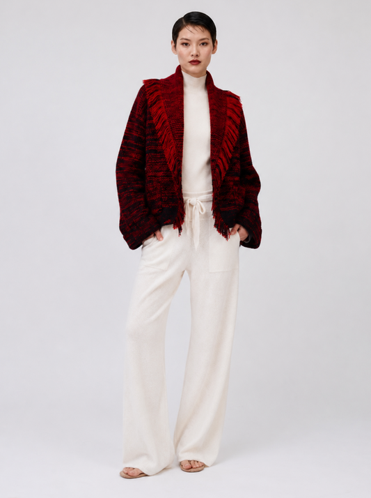 A model stands against a light gray studio background wearing a deep red textured open-front jacket over a white mock-neck top and white wide-leg trousers.